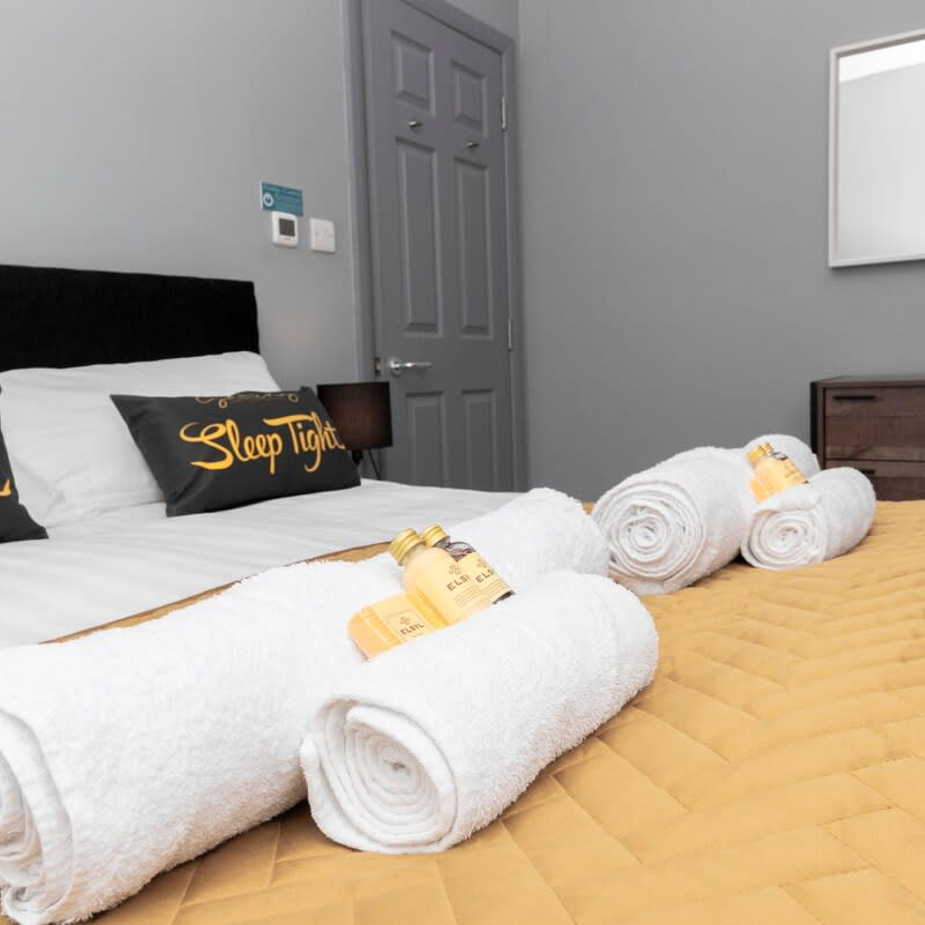 A hotel room with a bed, pillows, a nightstand, and rolled towels.