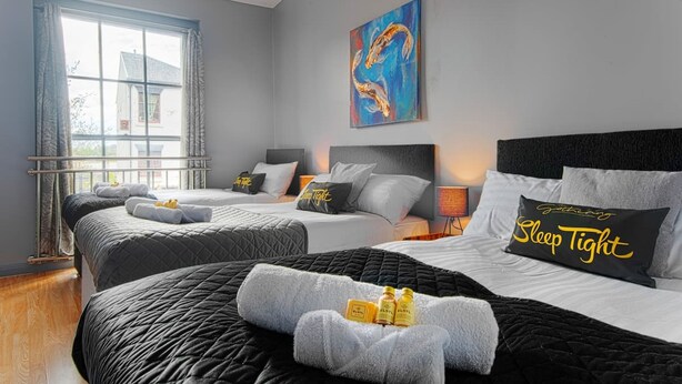 Une chambre d’hôtel avec deux lits, une grande fenêtre avec des rideaux, un tableau au mur et un oreiller orné de la phrase « Bonne nuit ».