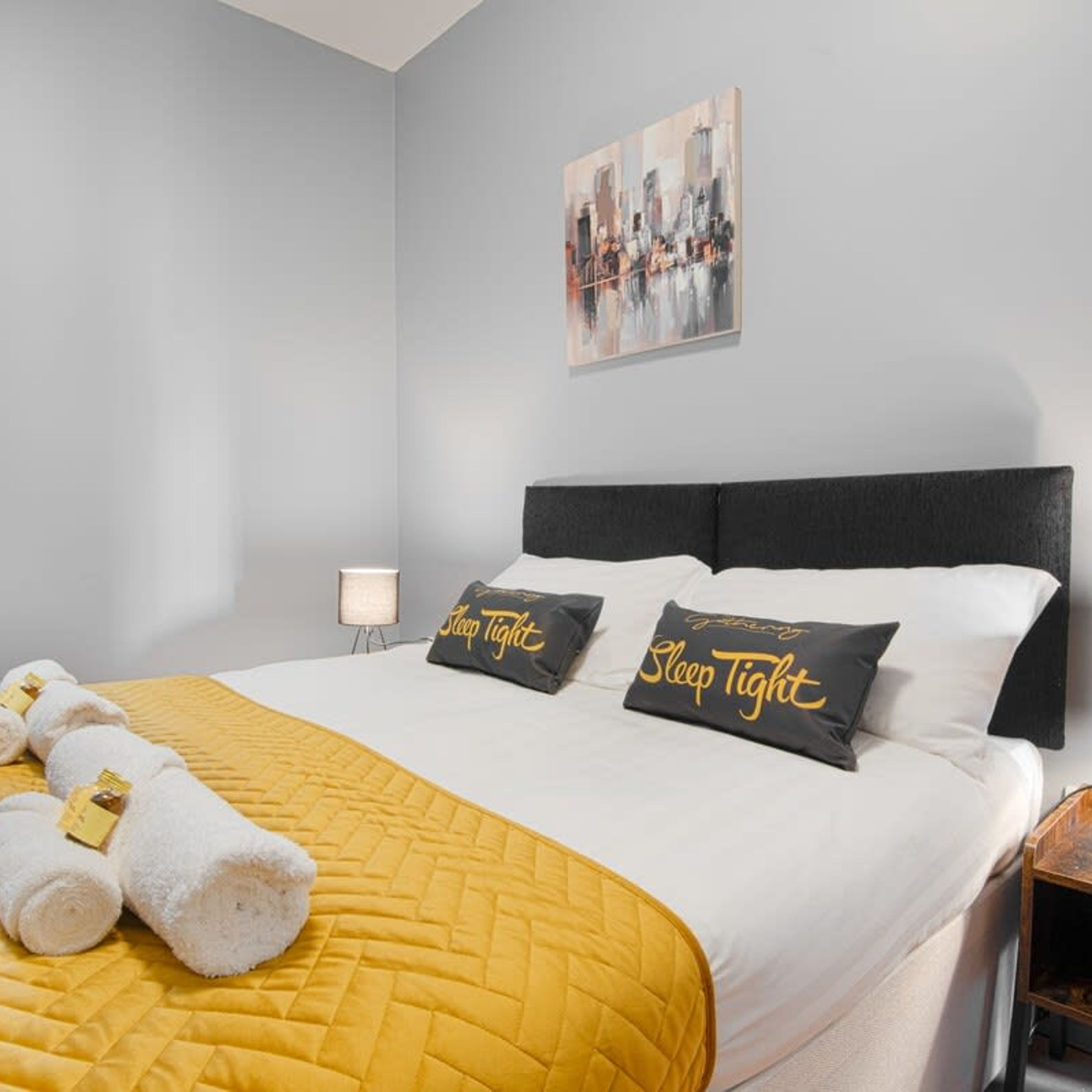 Una cama bien hecha con un edredón amarillo, dos almohadas con el texto 'Sleep Tight' y un cabecero.