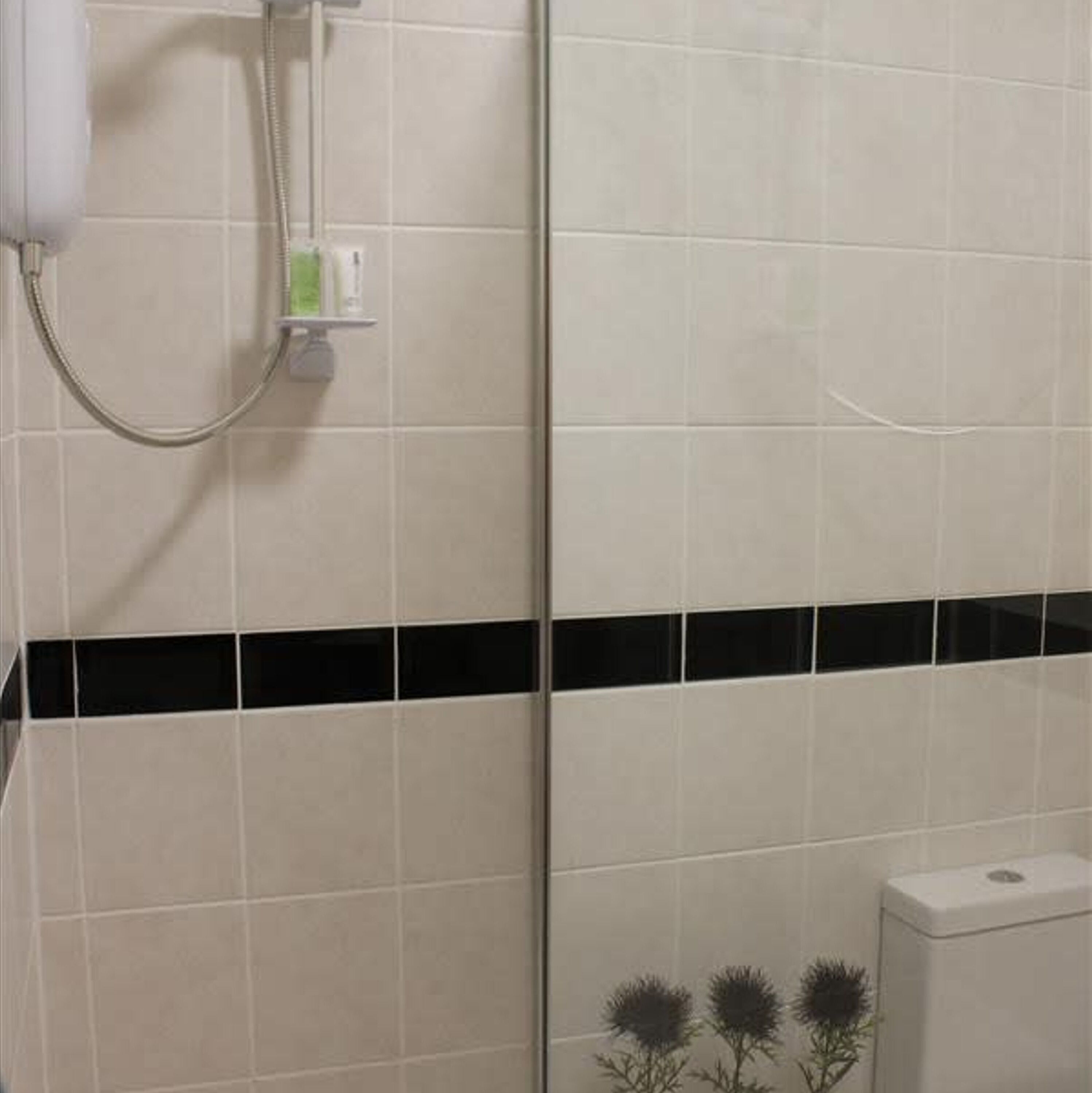 A bathroom with white tiles, a black horizontal stripe, and a shower with a hose.
