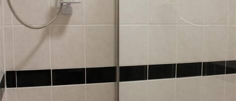 A bathroom with white tiles, a black horizontal stripe, and a shower with a hose.
