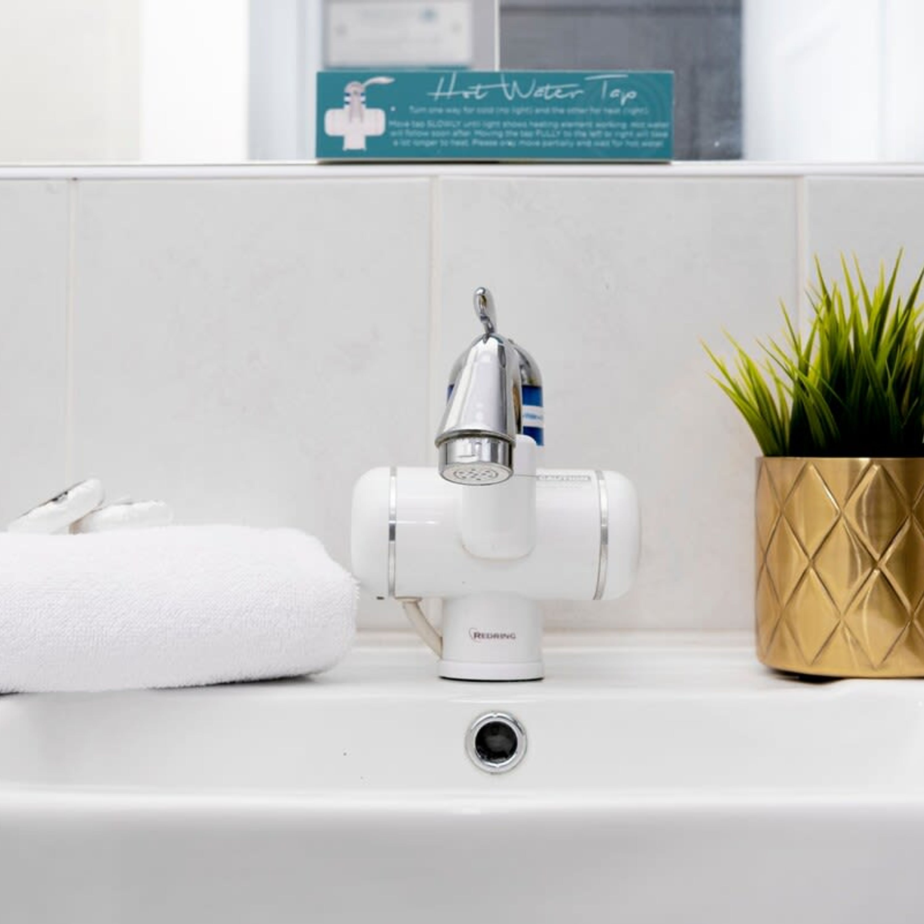 Un lavamanos de baño con un grifo de agua caliente, una toalla y una planta en maceta.