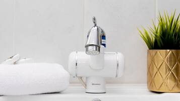 Un lavamanos de baño con un grifo de agua caliente, una toalla y una planta en maceta.