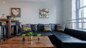 Uma sala de estar moderna com um sofá de couro preto, mesa de centro de madeira com plantas e obras de arte nas paredes.