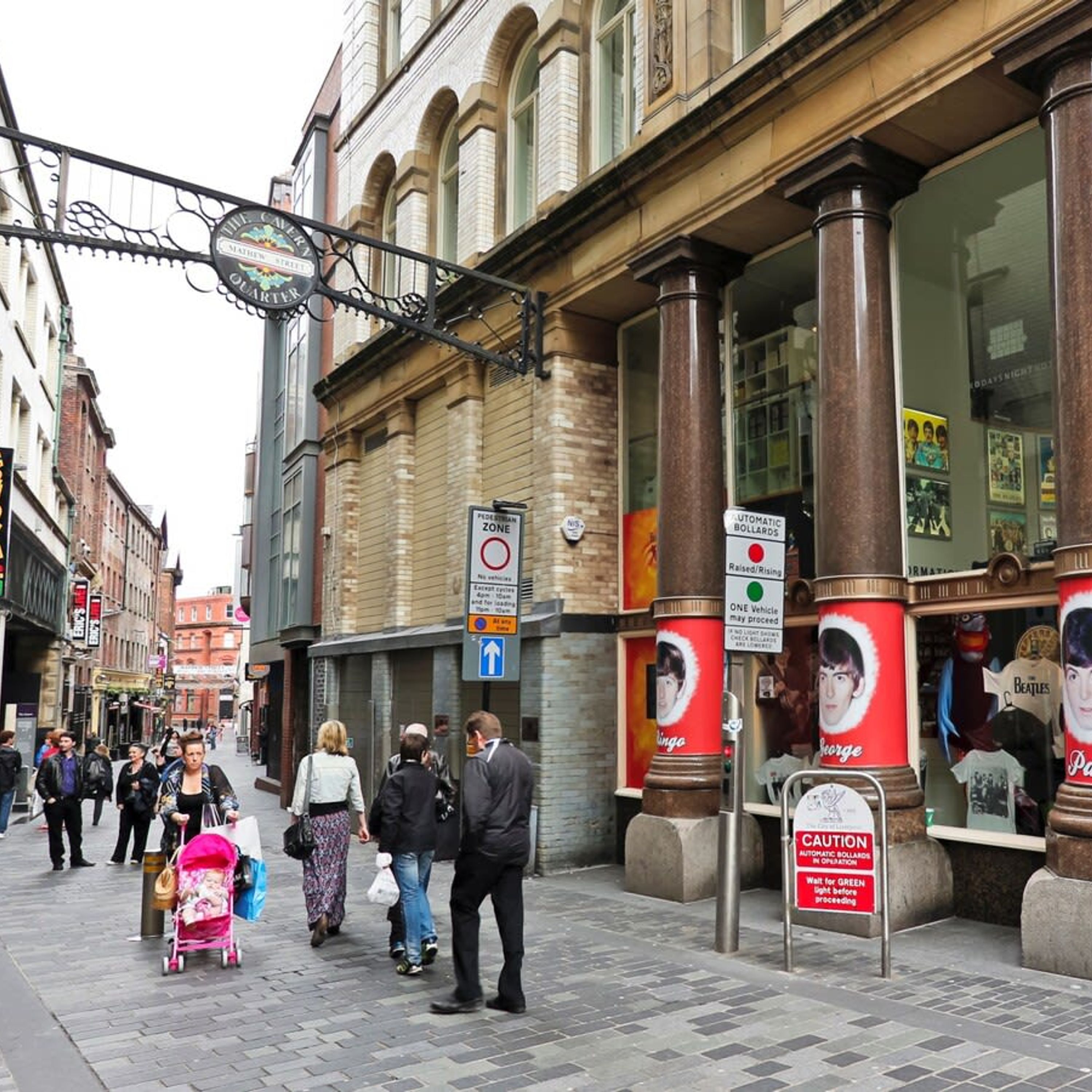 A busy urban street with pedestrians, a pedestrian zone sign, and a shop with Beatles memorabilia.