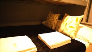 A single bed with a dark quilted bedspread, two pillows with leaf patterns, and a folded white towel on the bed. - The Mersey Apartment Liver House (Birkenhead)