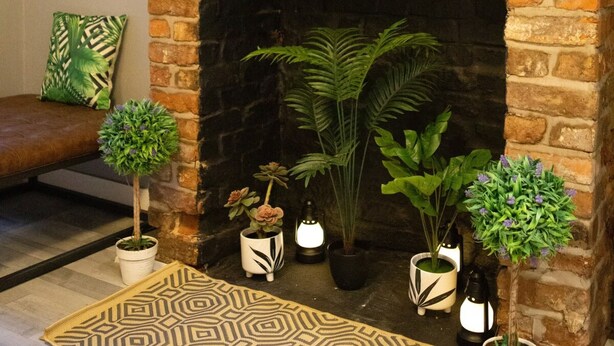 A cozy living room with a brick fireplace, a brown leather sofa, and various potted plants. - The Mersey Apartment Liver House (Birkenhead)