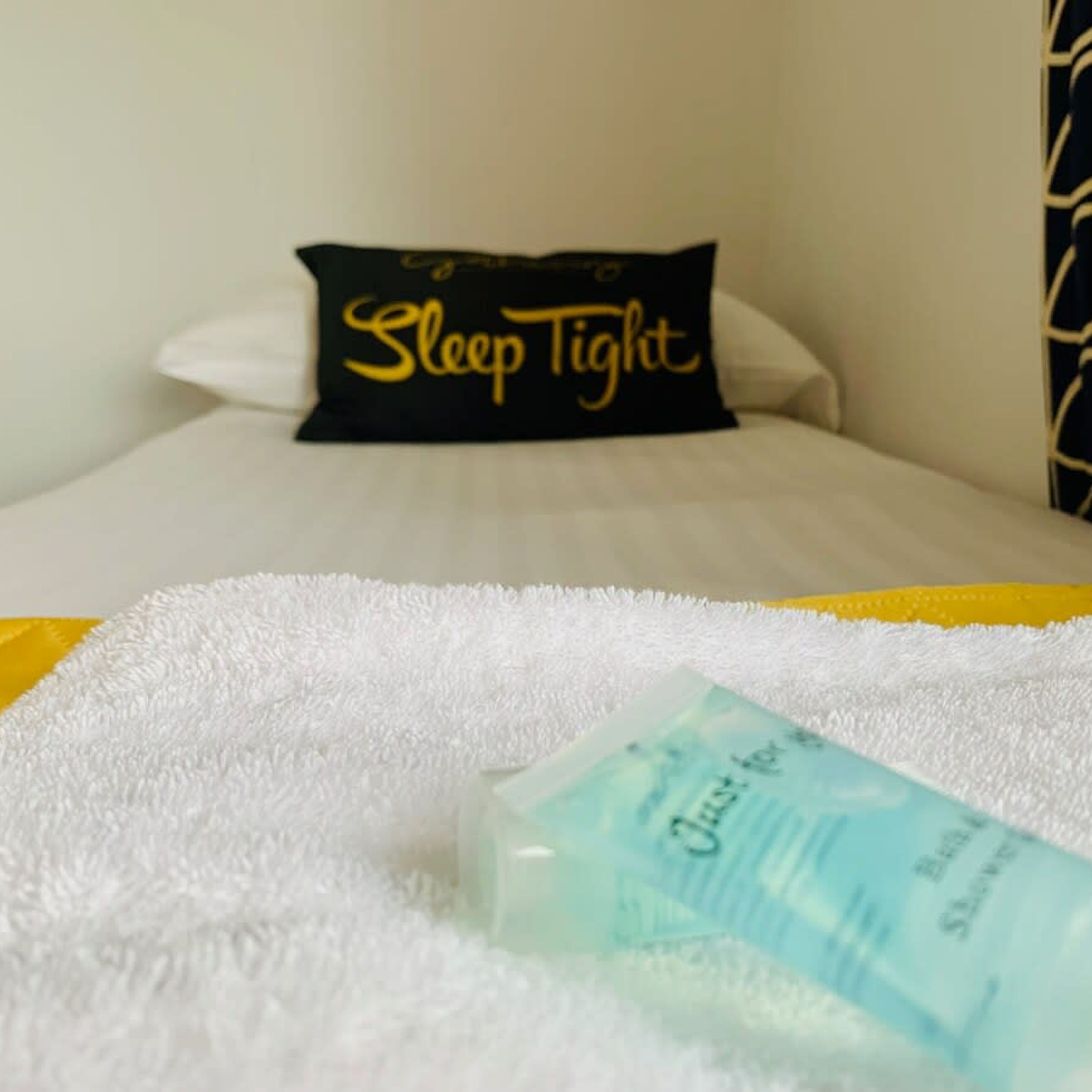A bed with a black pillow that reads "Sleep Tight" and a white fluffy blanket.