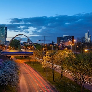 A cityscape with a prominent arch bridge, modern buildings, and a well-lit road with light trails.