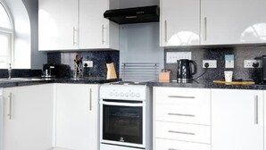 A modern kitchen with white cabinets, a black range hood, and a built-in oven.