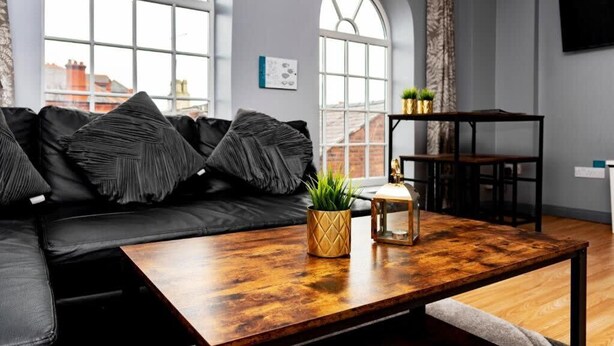 A modern living room with a black leather sofa, a wooden coffee table, and a small plant.