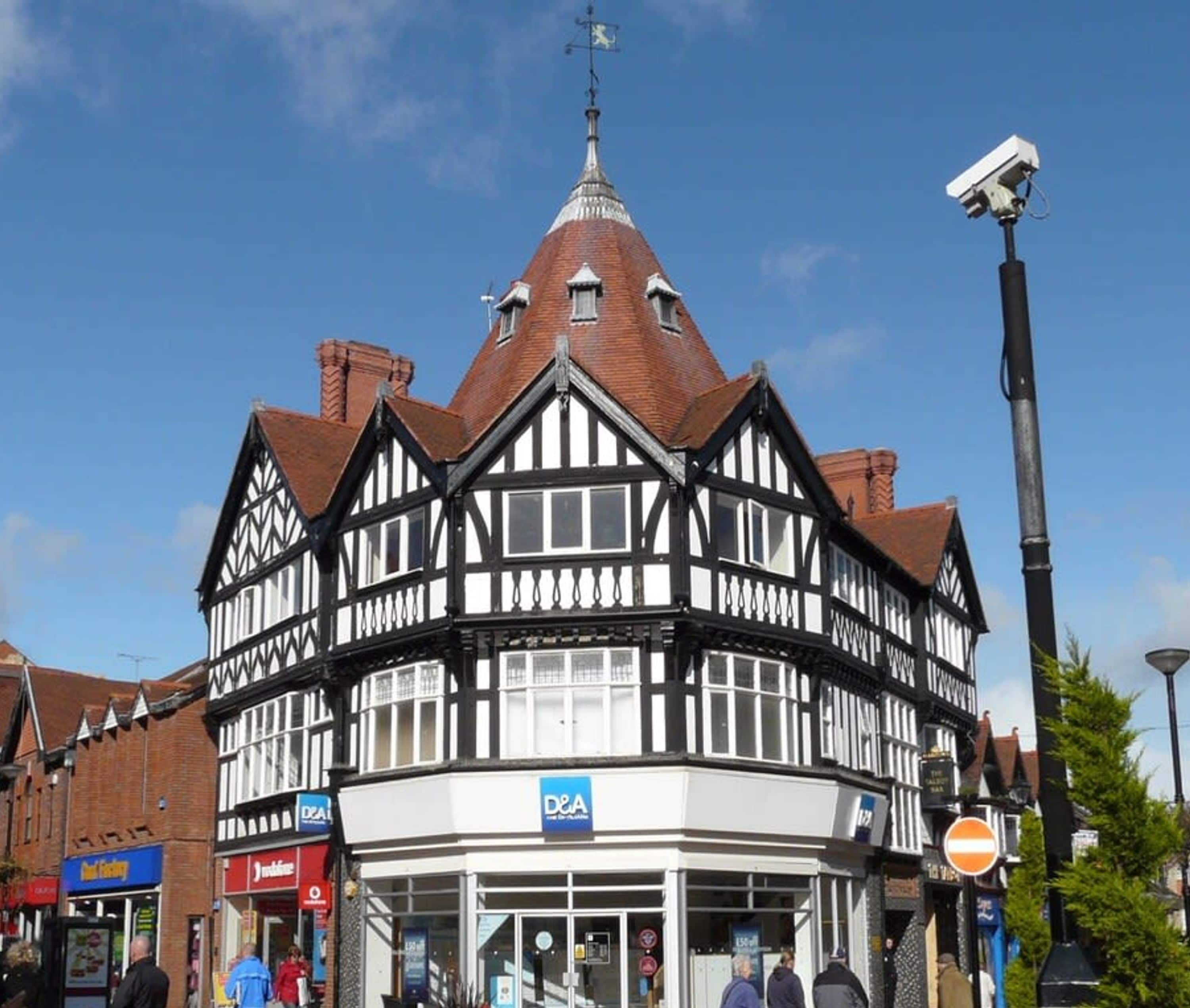 Un bâtiment de style Tudor traditionnel, doté d’une tour imposante, d’un magasin situé au rez-de-chaussée et surplombant un ciel d’un bleu éclatant.