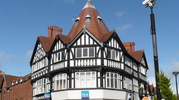 Un bâtiment de style Tudor traditionnel, doté d’une tour imposante, d’un magasin situé au rez-de-chaussée et surplombant un ciel d’un bleu éclatant.