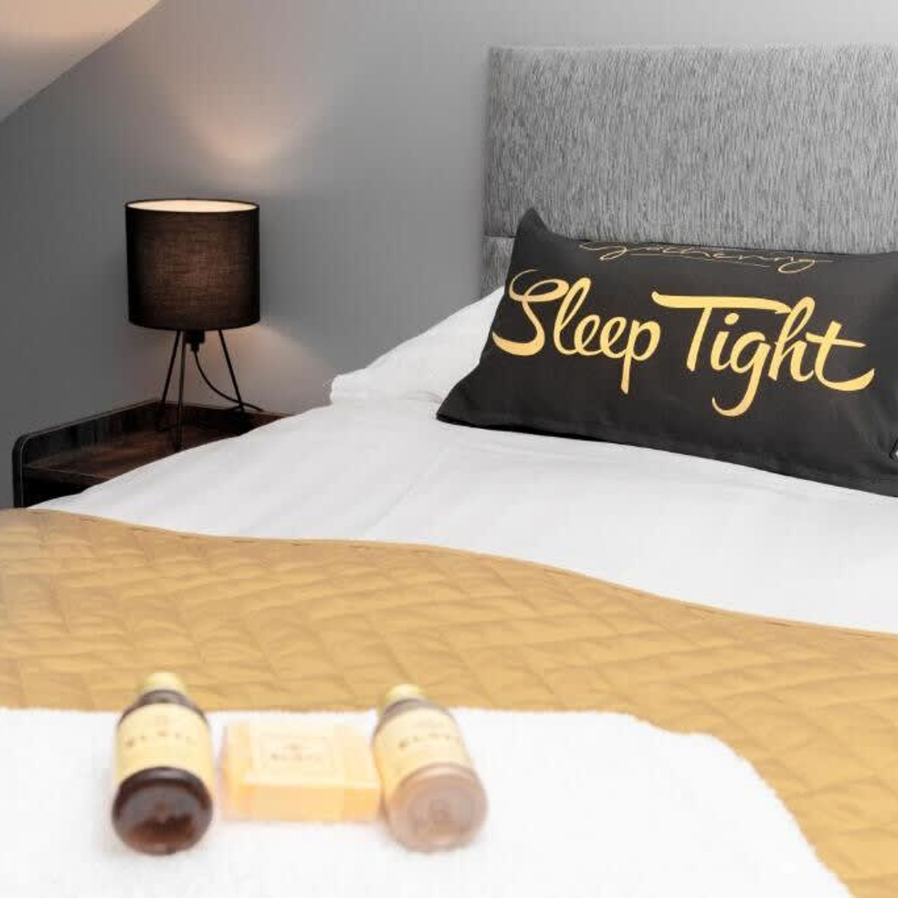 A neatly made bed with a pillow labeled "Sleep Tight" and two bottles on the bed.