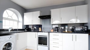 A modern kitchen with white cabinets, a built-in oven, a microwave, and a washing machine.