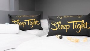 A bedroom with two black pillows with 'Sleep Tight' text, white bedding, and a wooden ceiling.