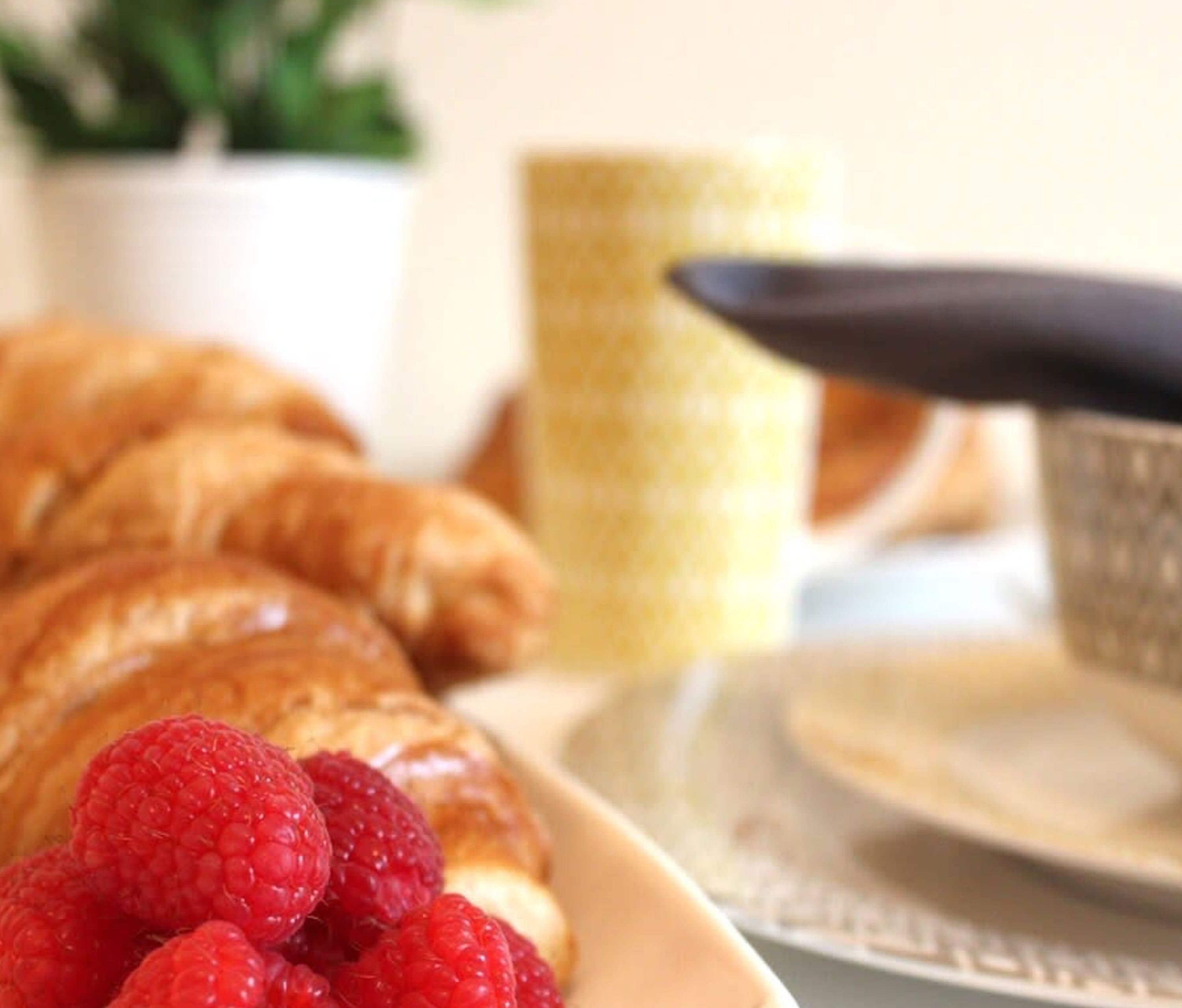 Une assiette avec des croissants et des framboises, une tasse et une cuillère sur une table.