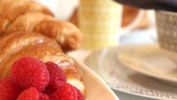 Une assiette avec des croissants et des framboises, une tasse et une cuillère sur une table.