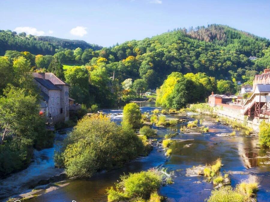Un río serpentea por un pueblo con edificios históricos y abundante vegetación.