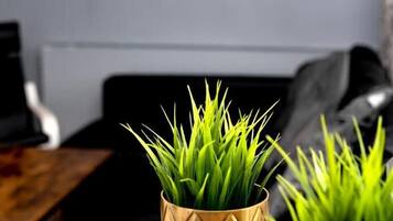 Una habitación con una mesa de madera, un sofá y dos plantas en macetas dentro de jarrones dorados.