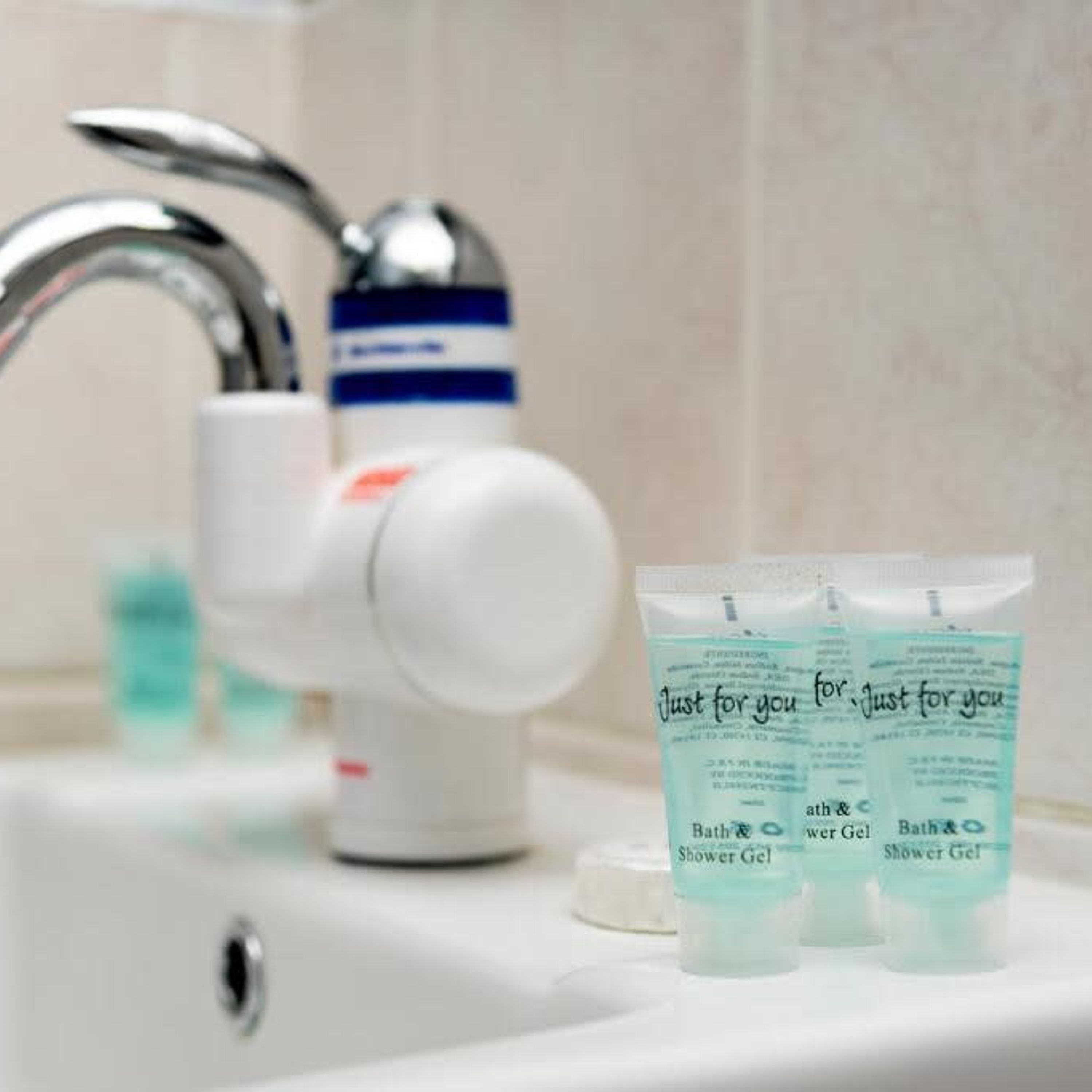 A bathroom sink with a faucet, a soap dispenser, and three tubes of shower gel labeled "Just for you".