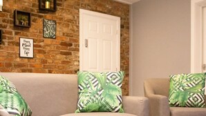 Una sala de estar con pared de ladrillo, una puerta blanca y dos sofás con cojines estampados verdes.
