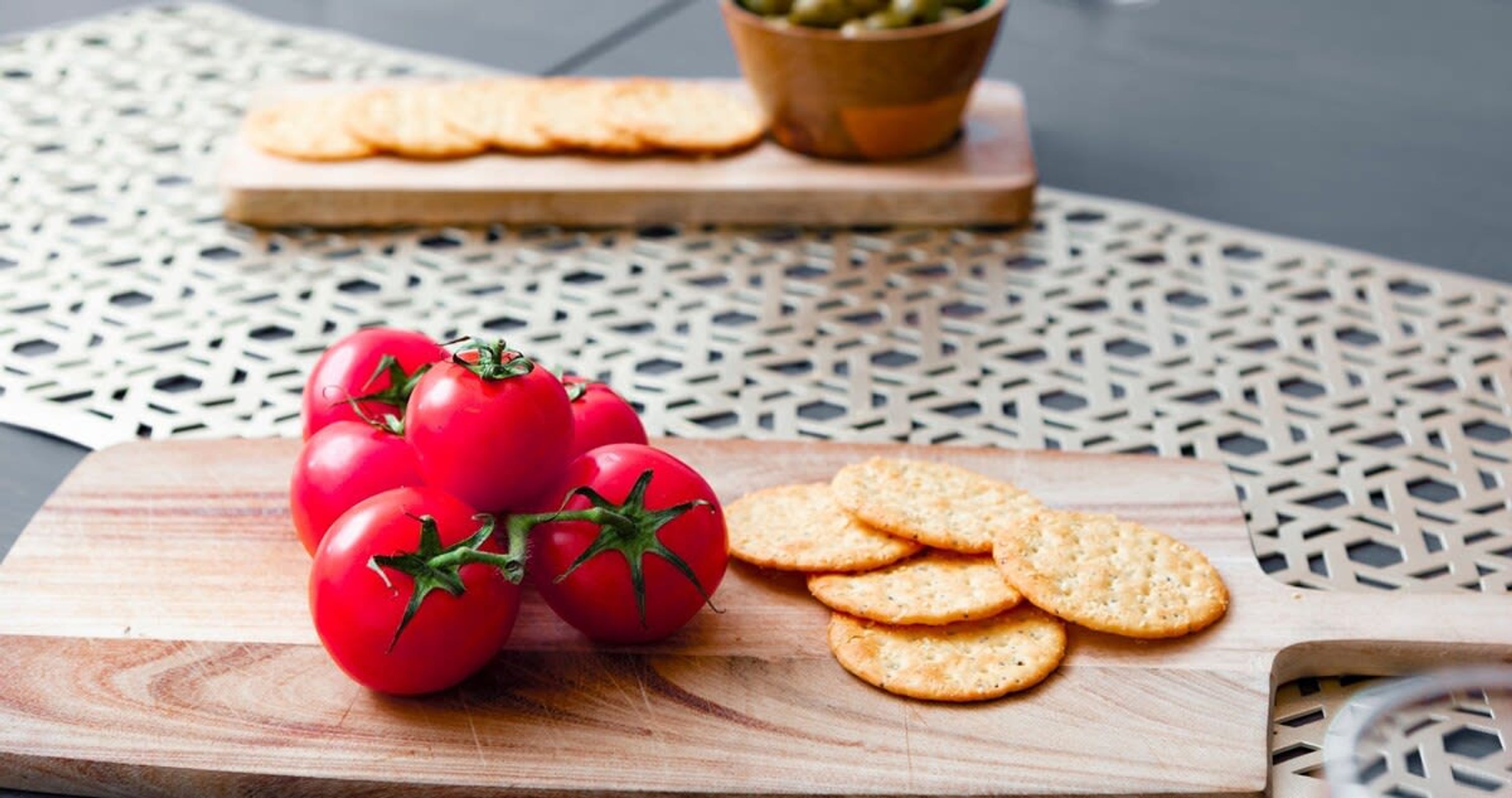 A wooden cutting board with tomatoes and crackers on a table with a geometric pattern.