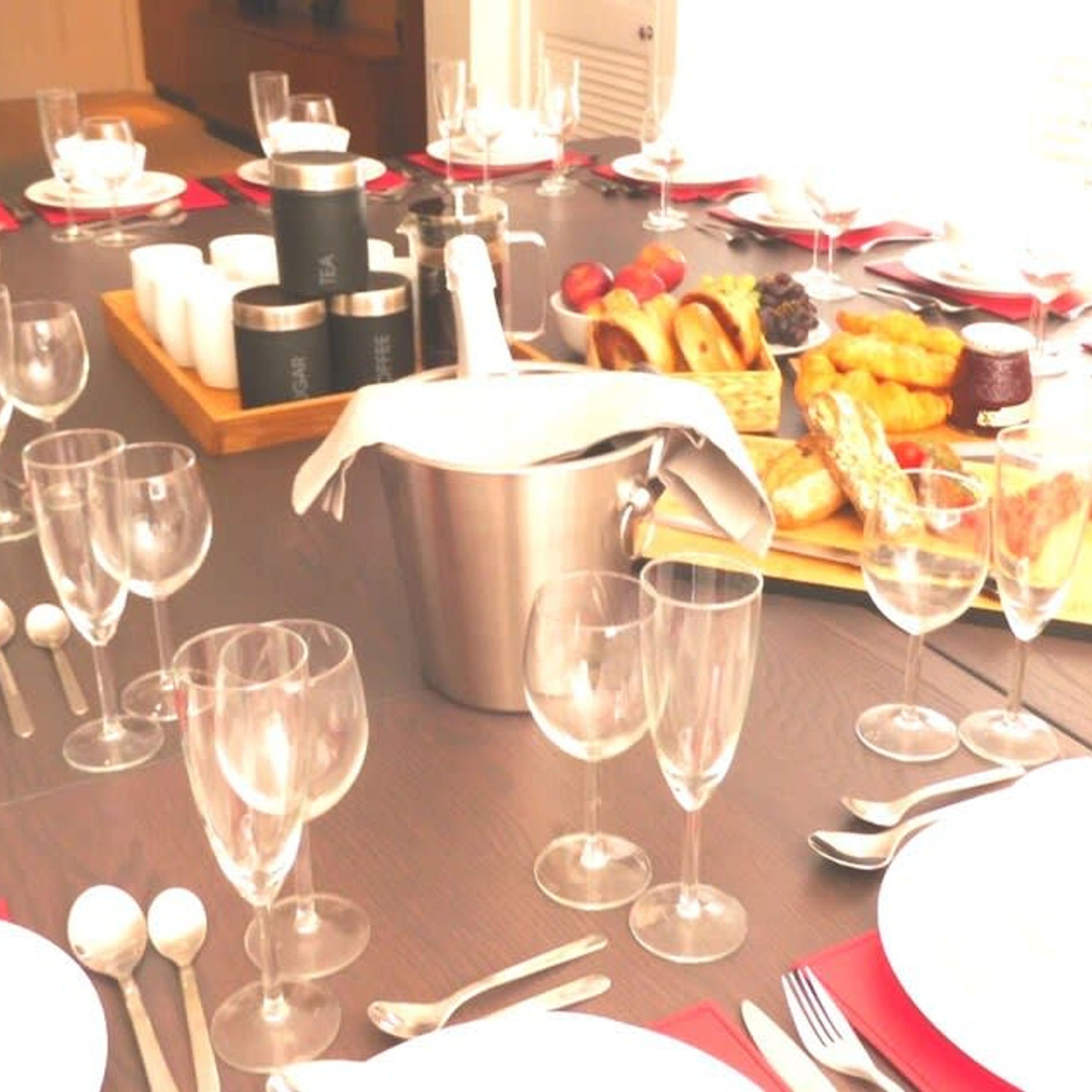 Una mesa de comedor dispuesta con copas de vino, platos, cubiertos y una variedad de alimentos.
