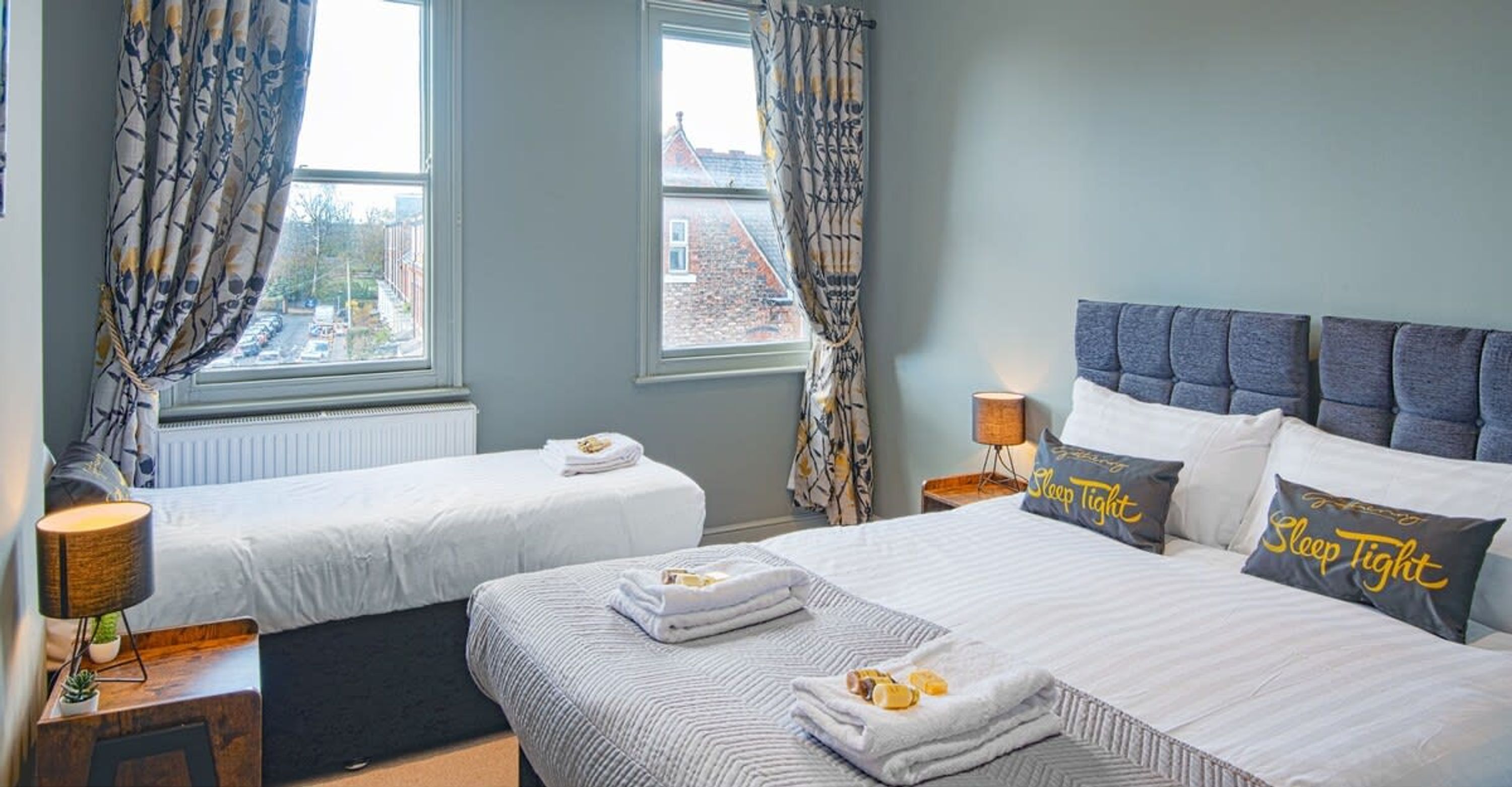 A hotel room with two beds, a view of the city, and a 'Sleep Tight' pillow.