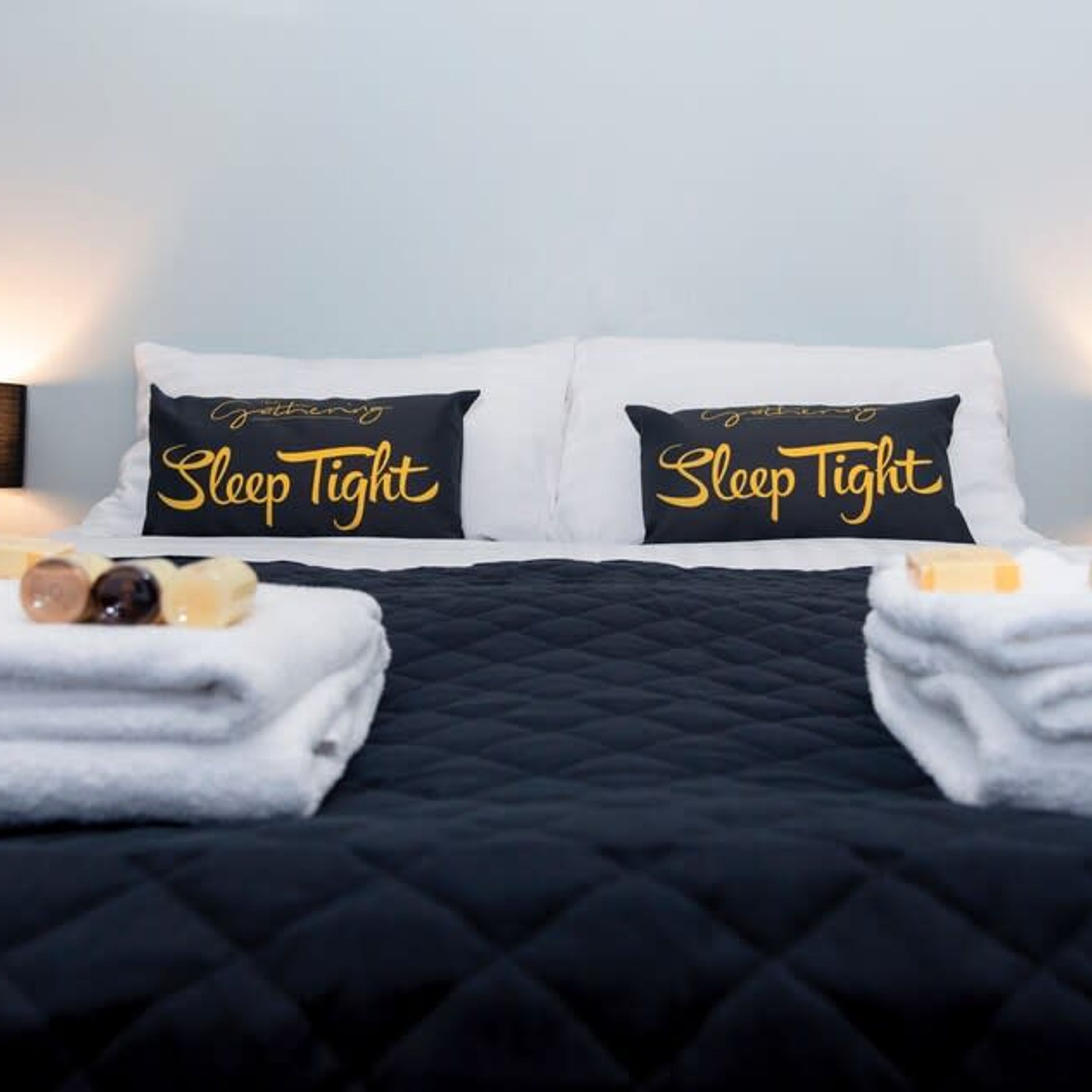 A neatly made bed with two pillows labeled "Sleep Tight" and a black quilted bedspread.