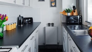 Cocina compacta con armarios blancos, una encimera negra, un tostador, un hervidor, un horno tostador y un lavabo.
