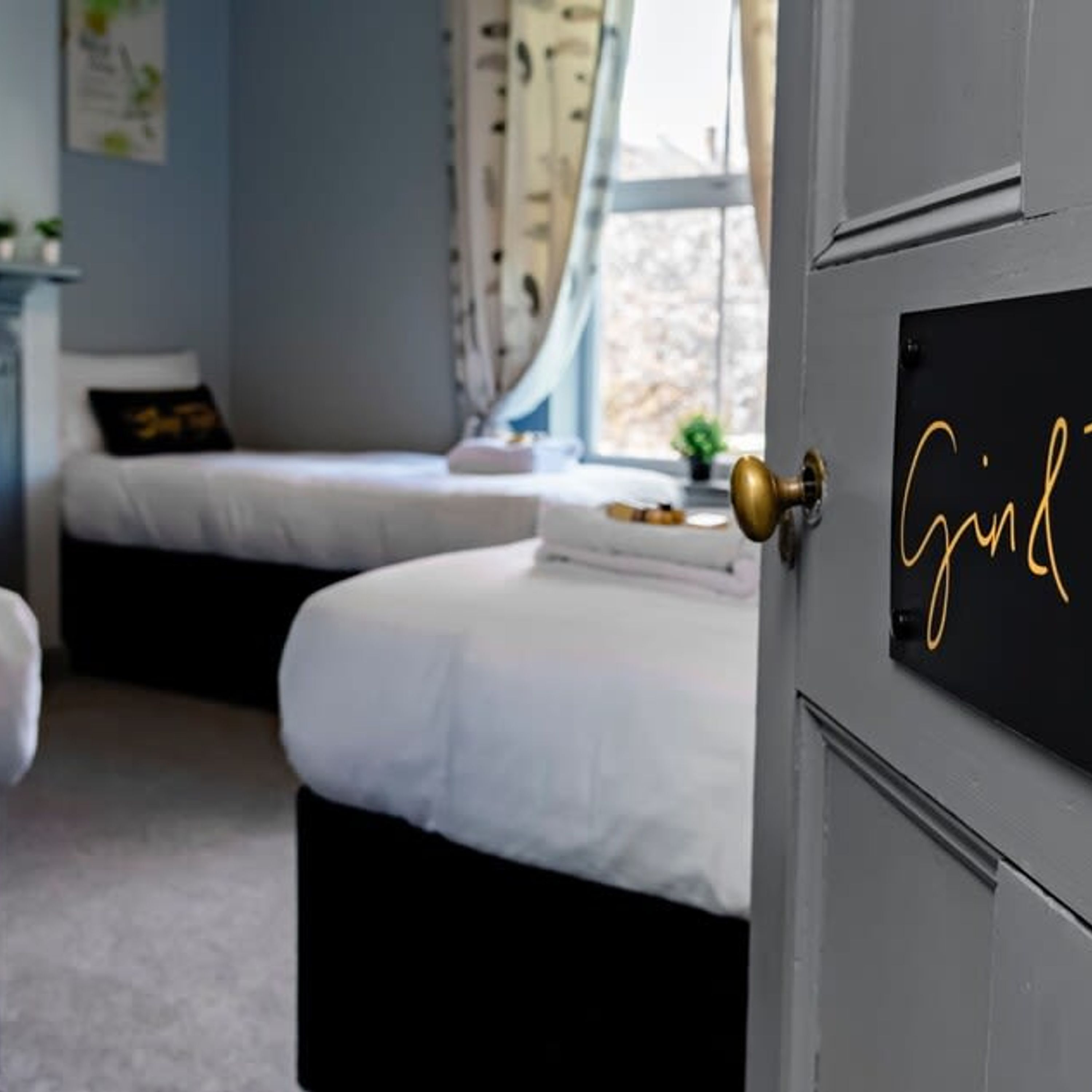 Un dormitorio con dos camas, una puerta con placa identificativa y una ventana con cortinas.