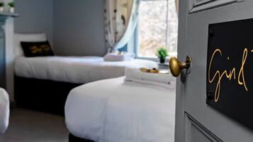 Un dormitorio con dos camas, una puerta con placa identificativa y una ventana con cortinas.