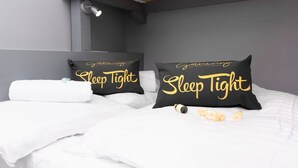 A neatly made bed with two black pillows featuring the text "Sleep Tight" in gold lettering, a white towel, and a small bottle of lotion on the bed. - The Lower Gathering - Wrexham Town Centre - Sleeps Up To 10 (Wrexham)
