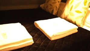 A bed with a dark quilted cover, two pillows with leaf patterns, and a folded white towel on the bed. - Paul s Studio Liver House (Birkenhead)