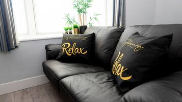 A black leather sofa with gold lettering pillows that say "Relax" and "Gathering."