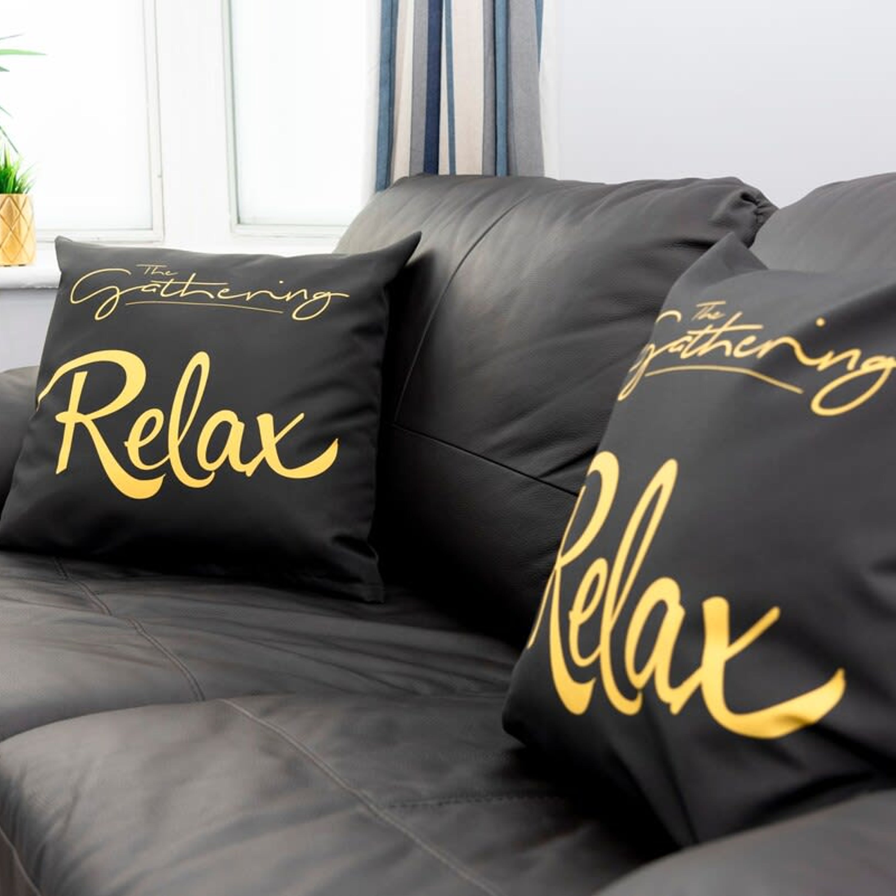 Un canapé en cuir noir avec deux coussins ornés de l’inscription « The Gathering Relax ».