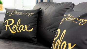 Un canapé en cuir noir avec deux coussins ornés de l’inscription « The Gathering Relax ».