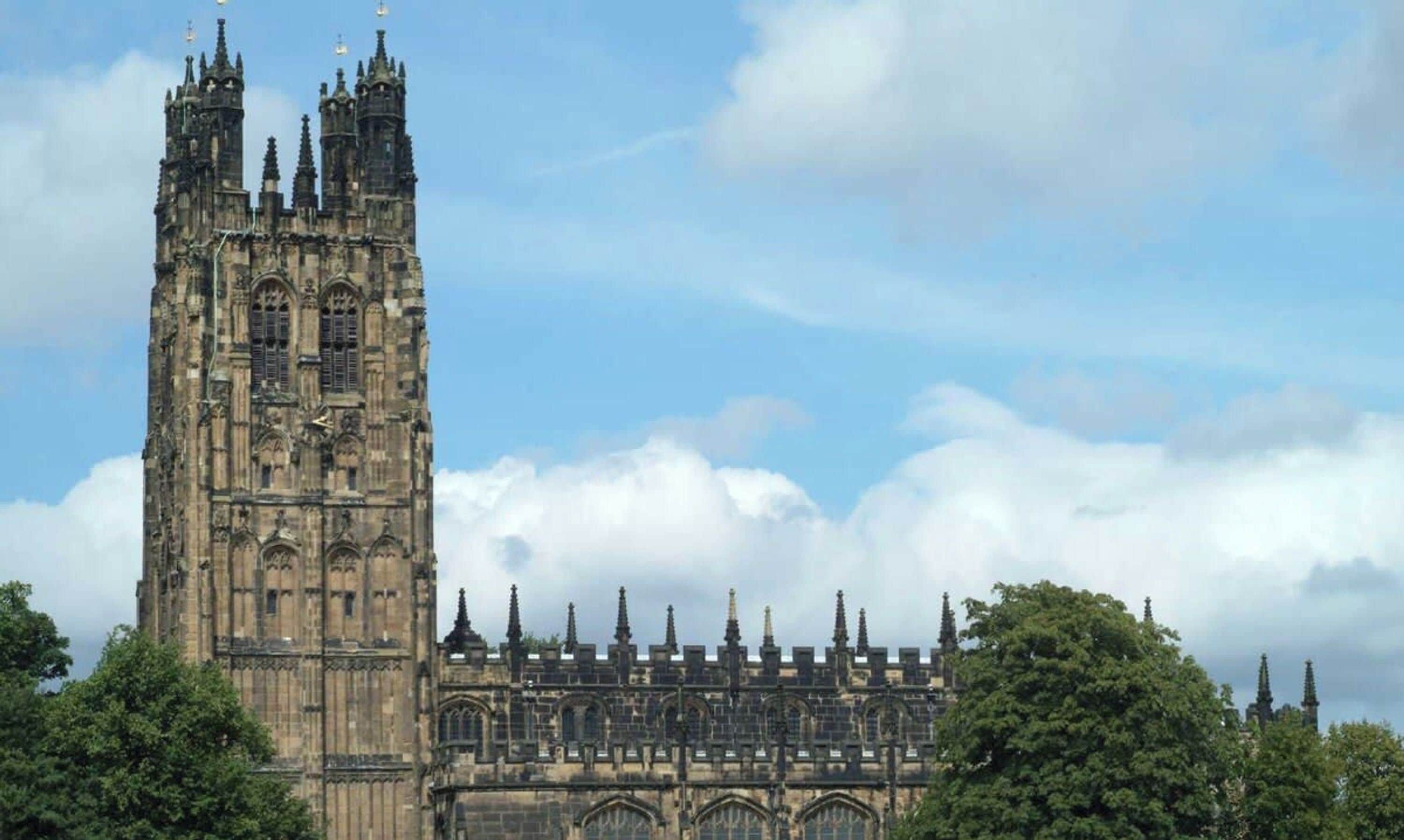 Un edificio histórico con una torre alta y múltiples agujas, rodeado de árboles.