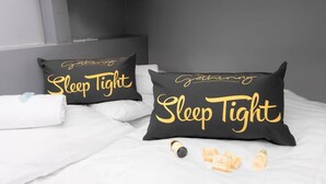 A bed with two black pillows with 'Sleep Tight' text, a white towel, and a bottle of lotion. - Wrexham Central Stay Apartment Seven (Wrexham)