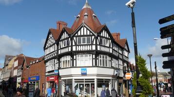 A traditional Tudor-style building with a prominent clock tower, a D&A sign, and a pedestrian area with shops and people.