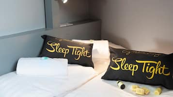 Een net opgemaakt bed met twee zwarte kussens met de tekst 'Sleep Tight' en een witte handdoek.
