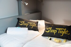 A neatly made bed with two black pillows labeled "Sleep Tight" and a white towel.