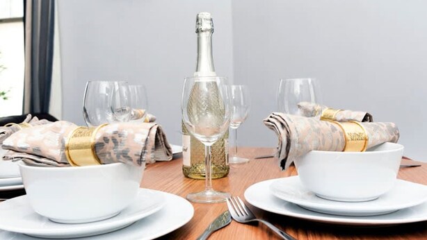 A dining table set with white plates, bowls, and cutlery, a bottle of wine, and a glass. - Wrexham Central Stay Apartment Seven (Wrexham)