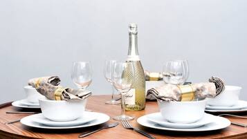 Ett runt matbord dukat med vita tallrikar, skålar och bestick, en flaska champagne och glas.