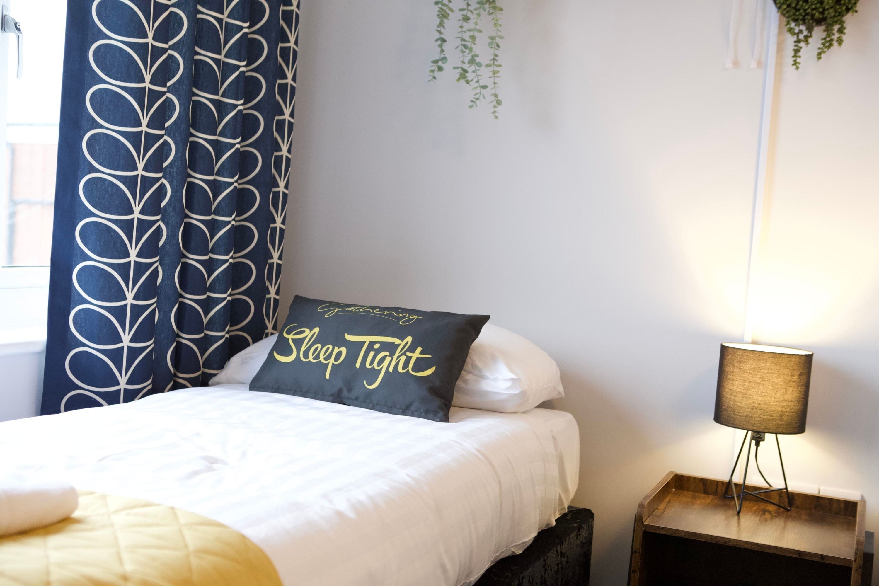Een keurig opgemaakt bed met een sierkussen waarop staat 'Slaap lekker' en een bedlampje op een houten nachtkastje.
