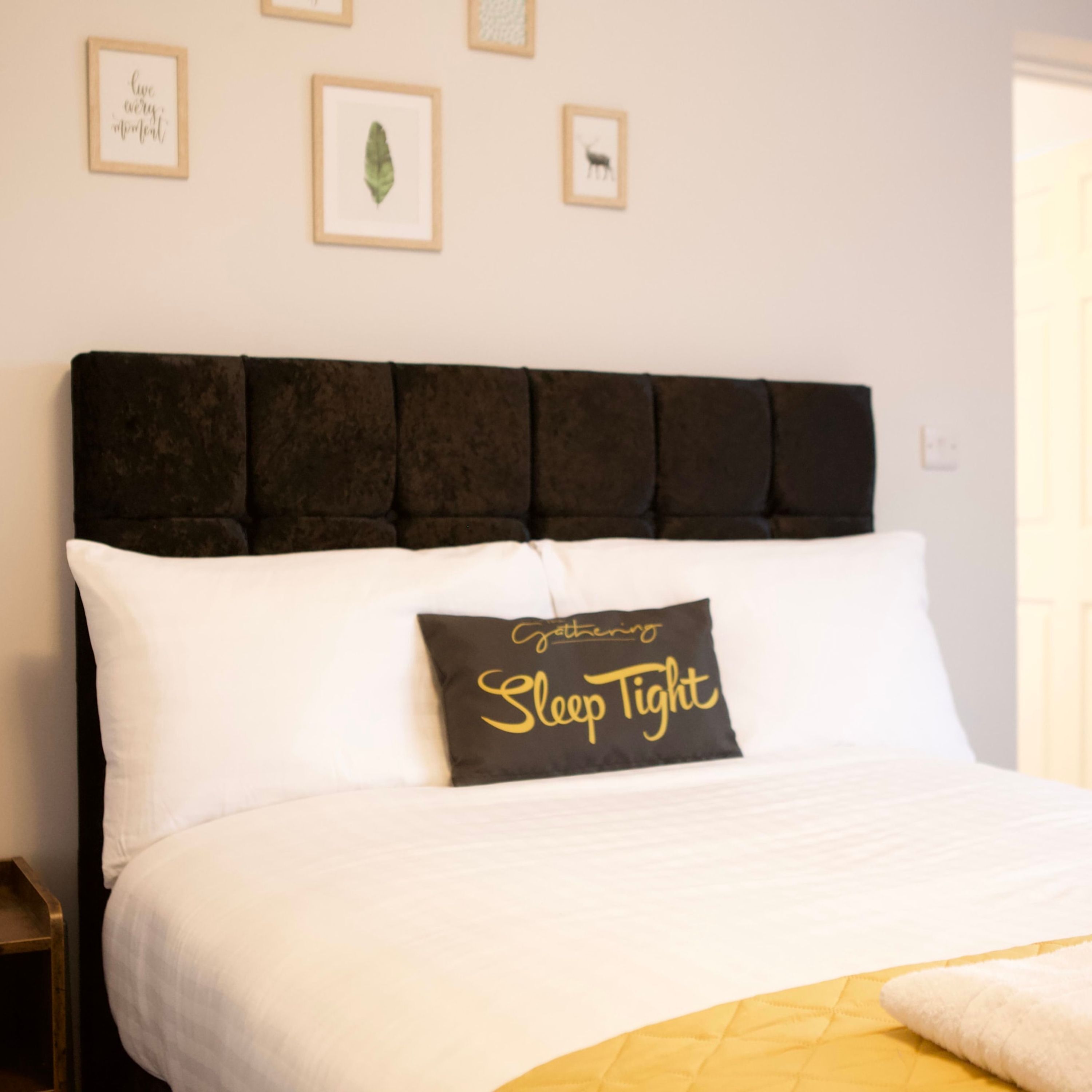 Una cama con cabecera negra, almohadas blancas y una almohada negra con la frase 'gathering Sleep Tight'.