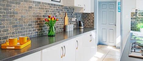 A modern kitchen with white cabinets, a black countertop, and a tiled backsplash. There is a coffee maker, a kettle, and a tray with orange cups.