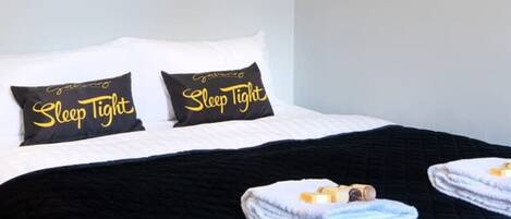 A neatly made bed with black and white bedding, two pillows with 'Sleep Tight' text, and folded towels on the bed.