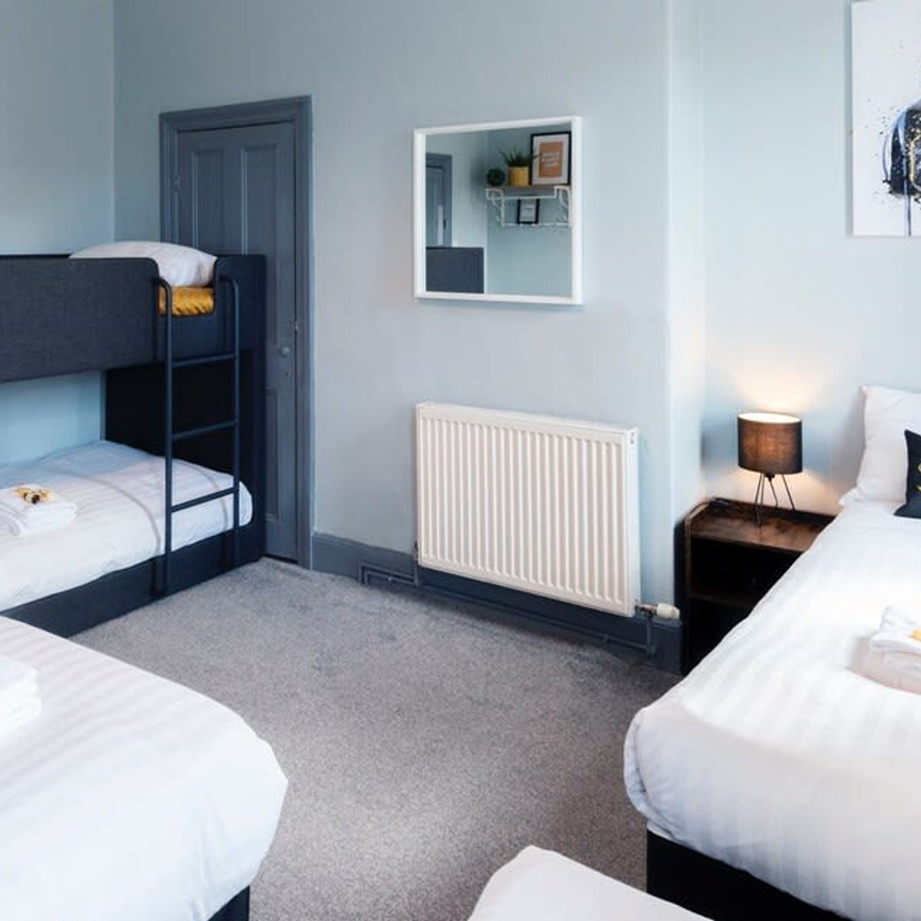 A room with bunk beds, a radiator, a bedside lamp, and a mirror on the wall.